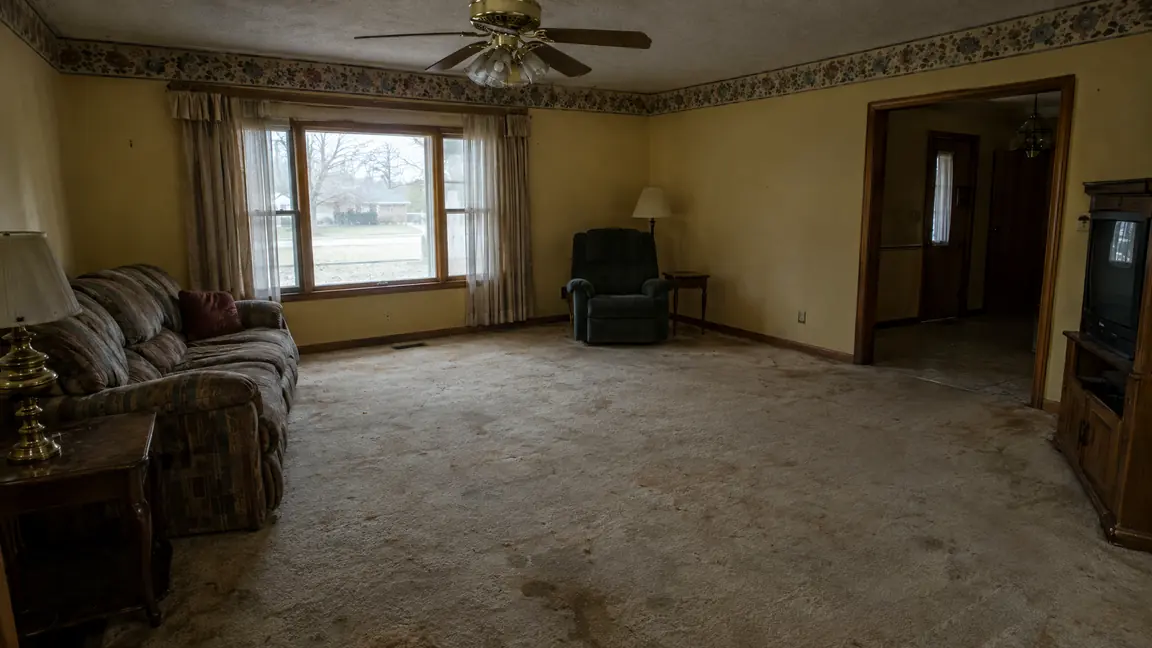 Before: Worn Carpet | Music City Remodels Before: A dim living room with worn stained beige carpet, dated wallpaper border, brass ceiling fan and dull yellow walls