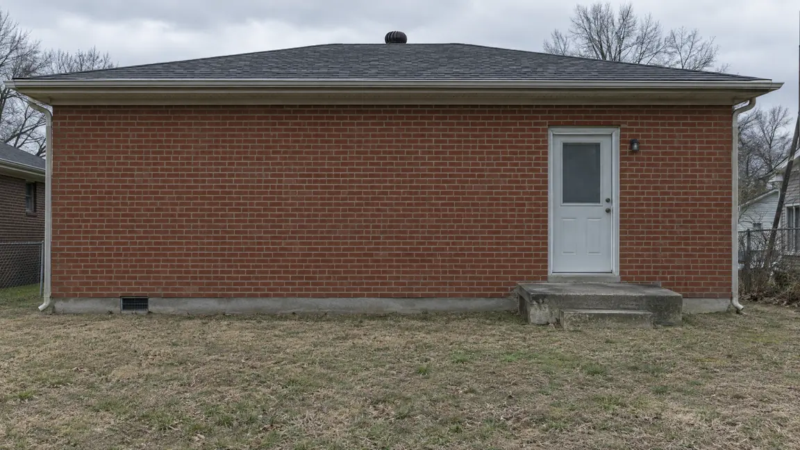 Before: Bare Backyard | Music City Remodels Before: The back of a brick home with a plain back wall, a small concrete stoop, a bare lawn and a single door, flat gray lighting