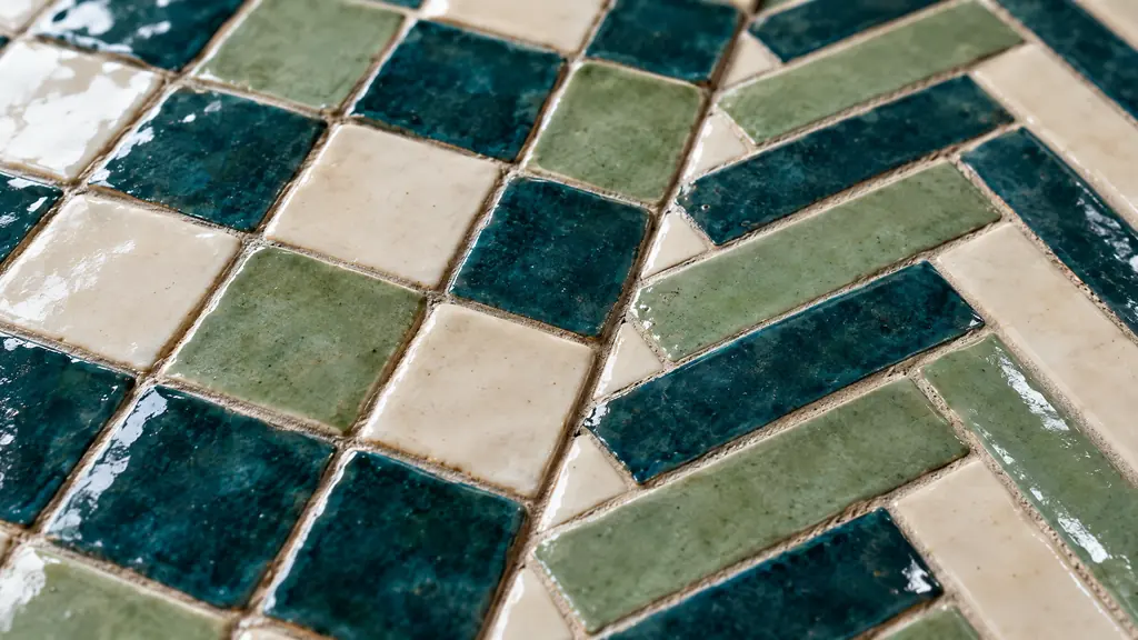 A macro close-up of handmade zellige and herringbone ceramic tiles in deep teal, cream and soft green glazes with subtle shine, shallow depth of field